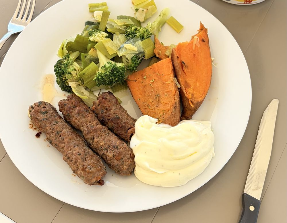 Ein Teller mit Gemüse, Hackfleischröllchen, Süßkartoffel und Joghurt-Dip